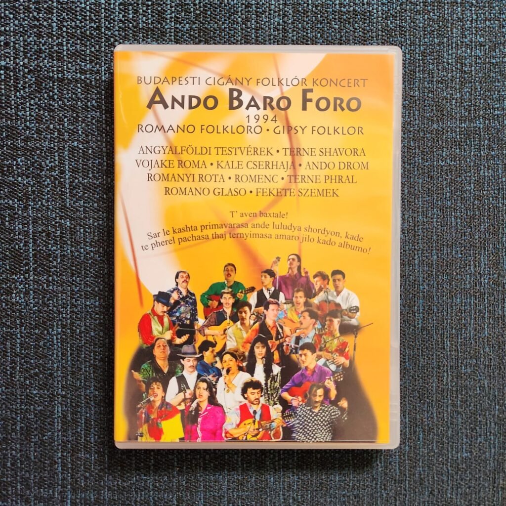 Cover of Ando Baro Foro 1994 — Budapesti Cigány Folklór Koncert, with an orange background, the names of participating Roma ensembles, Romani-language text, and a montage of musicians and singers.